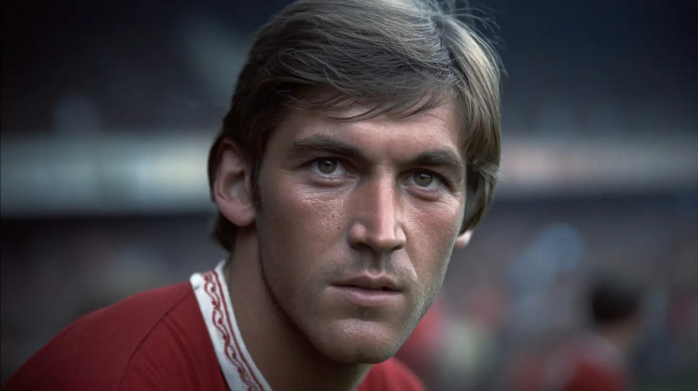 Kenny Dalglish wearing a red Liverpool football shirt with a white patterned collar, close-up portrait with blurred stadium background.