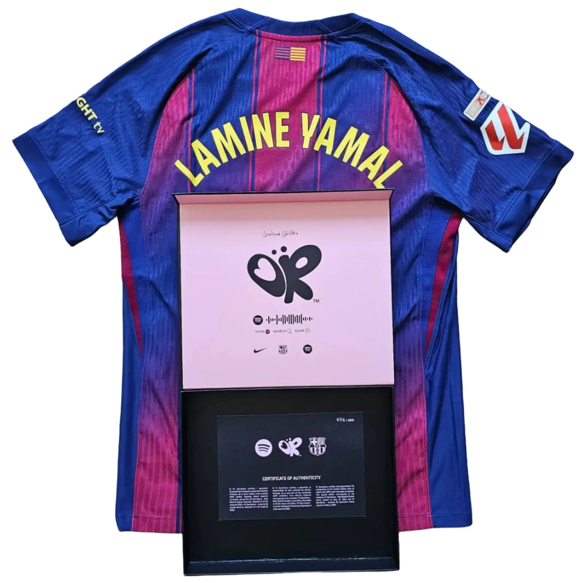A blue and magenta FC Barcelona-style soccer jersey with 'LAMINE YAMAL' printed across the back, laid flat on a wood floor with a pink and black framed award plaque in front.