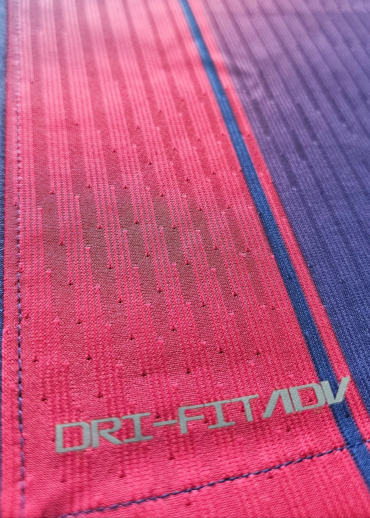 Close-up of a textured athletic fabric with a red-to-blue gradient and the visible text 'DRI-FIT ADV' near the bottom.
