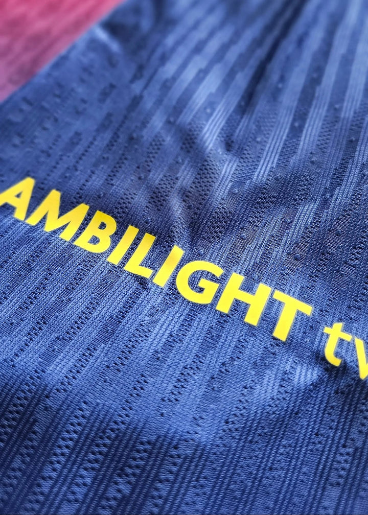 Close-up of the blue knit shirt with yellow AMBILIGHT TV text, a pink ribbed section visible at the corner.