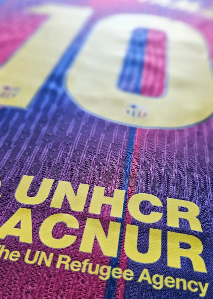 Yellow 'UNHCR ACNUR' sponsor lettering and a partial crest patch on maroon and navy striped fabric, from Lamine Yamal's 2025-2026 Barcelona number 10 shirt.