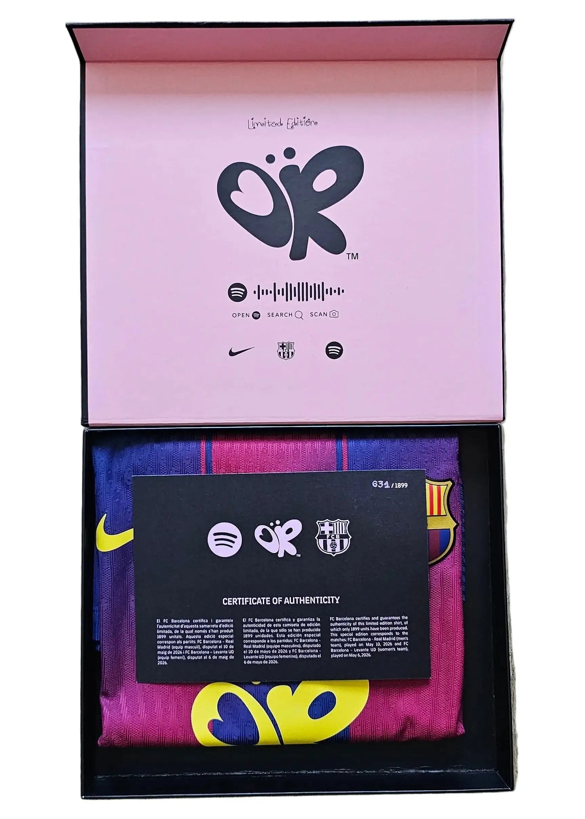 A luxury gift box set containing a folded FC Barcelona soccer jersey in its original pink and black packaging, displayed on a light wood floor. The box lid features the 'OR' logo and FC Barcelona branding.