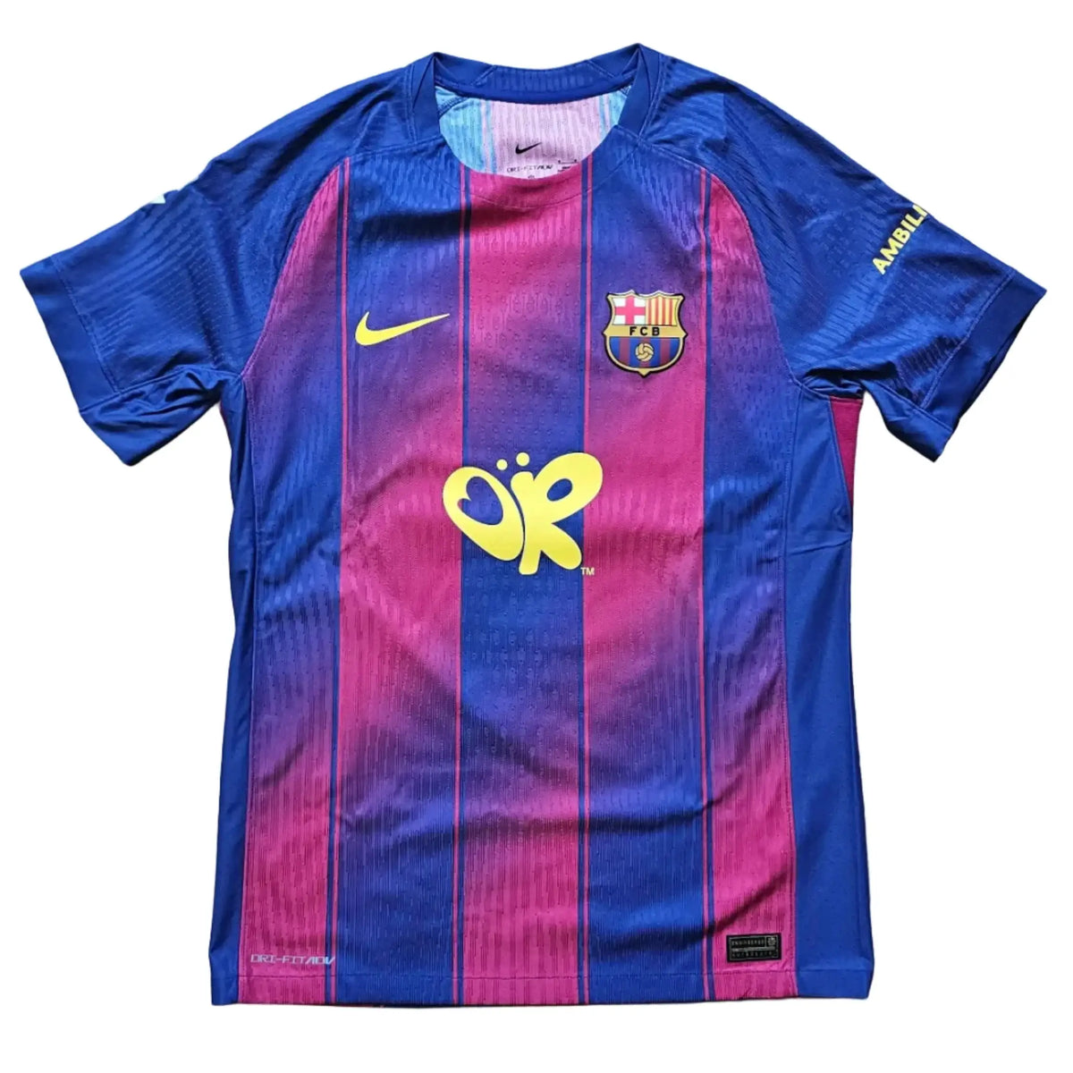 A Nike FC Barcelona home soccer jersey with blue and magenta vertical stripes, laid flat on a light wood floor. The jersey features the yellow 'Jupiler' sponsor logo on the center chest, a yellow Nike swoosh on the right chest, and the FC Barcelona crest on the left chest.