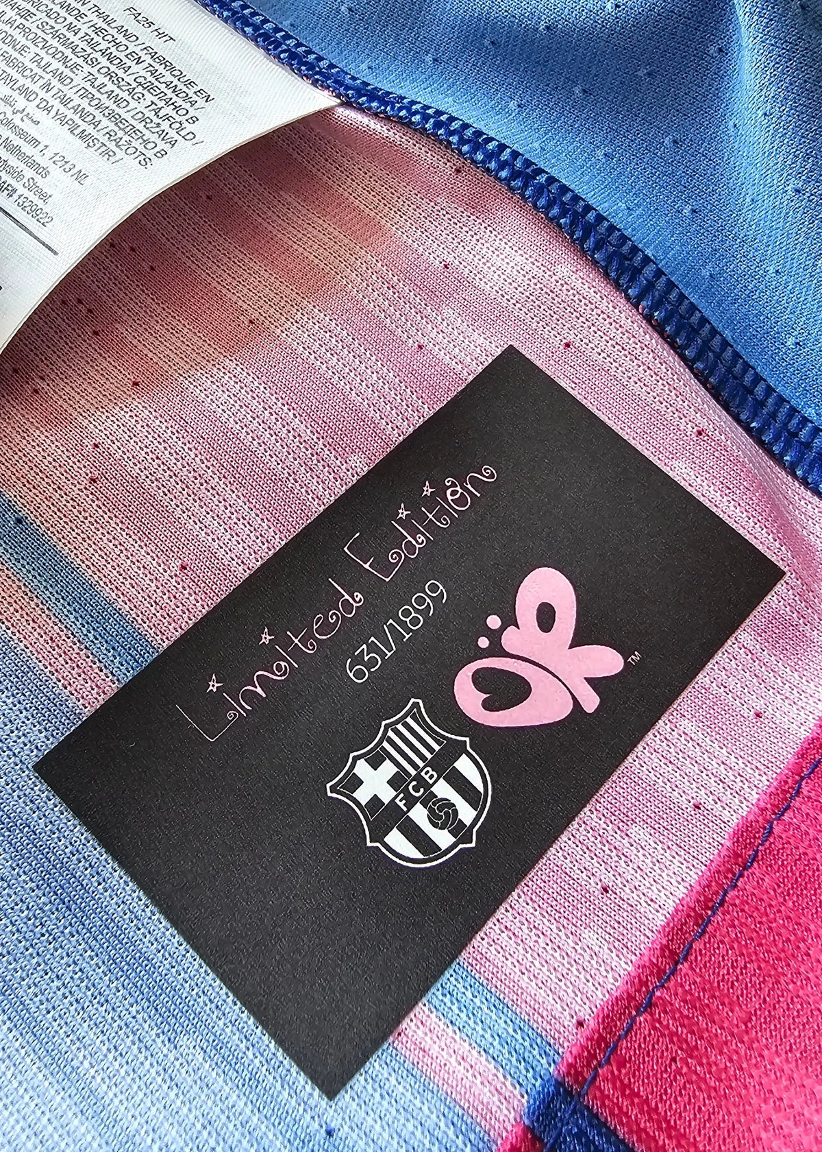 Close-up of striped knit fabric in pink, blue, and white with a black label reading Edition 650/199 and the FC Barcelona crest.