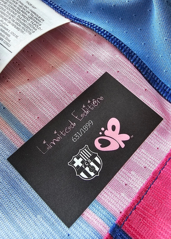 Close-up of striped knit fabric in pink, blue, and white with a black label reading Edition 650/199 and the FC Barcelona crest.