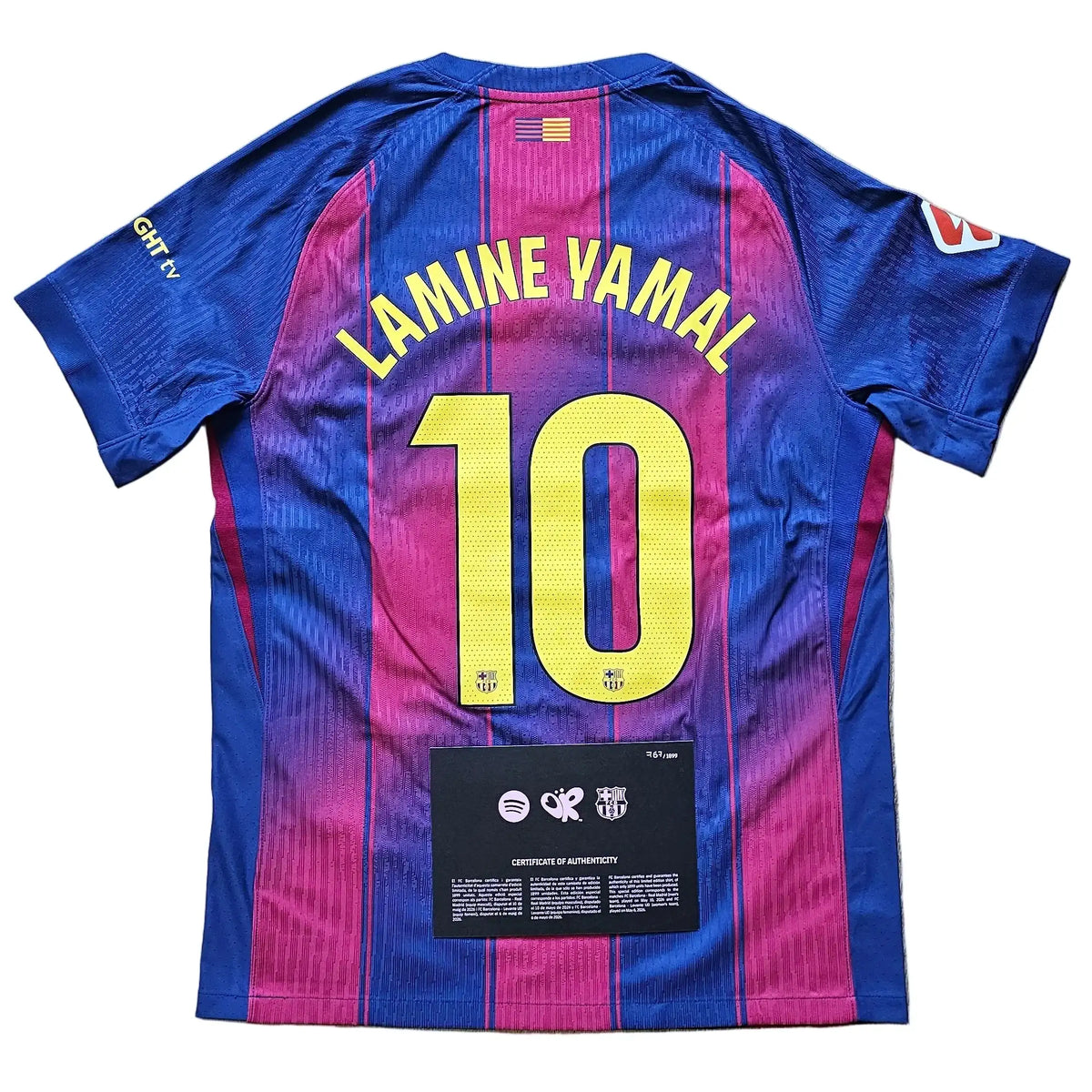 A FC Barcelona home jersey with the back of Lamine Yamal's name and number 10, laid flat on a light wood floor.