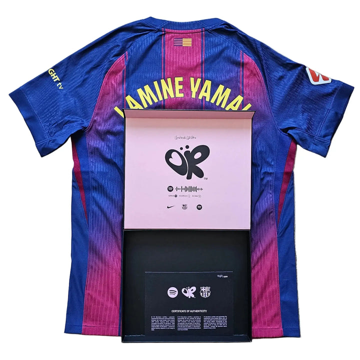 A blue and magenta gradient FC Barcelona soccer jersey with 'YAMINE YAMAL' on the back, laid flat on a gray wood floor with a pink and black presentation box underneath.