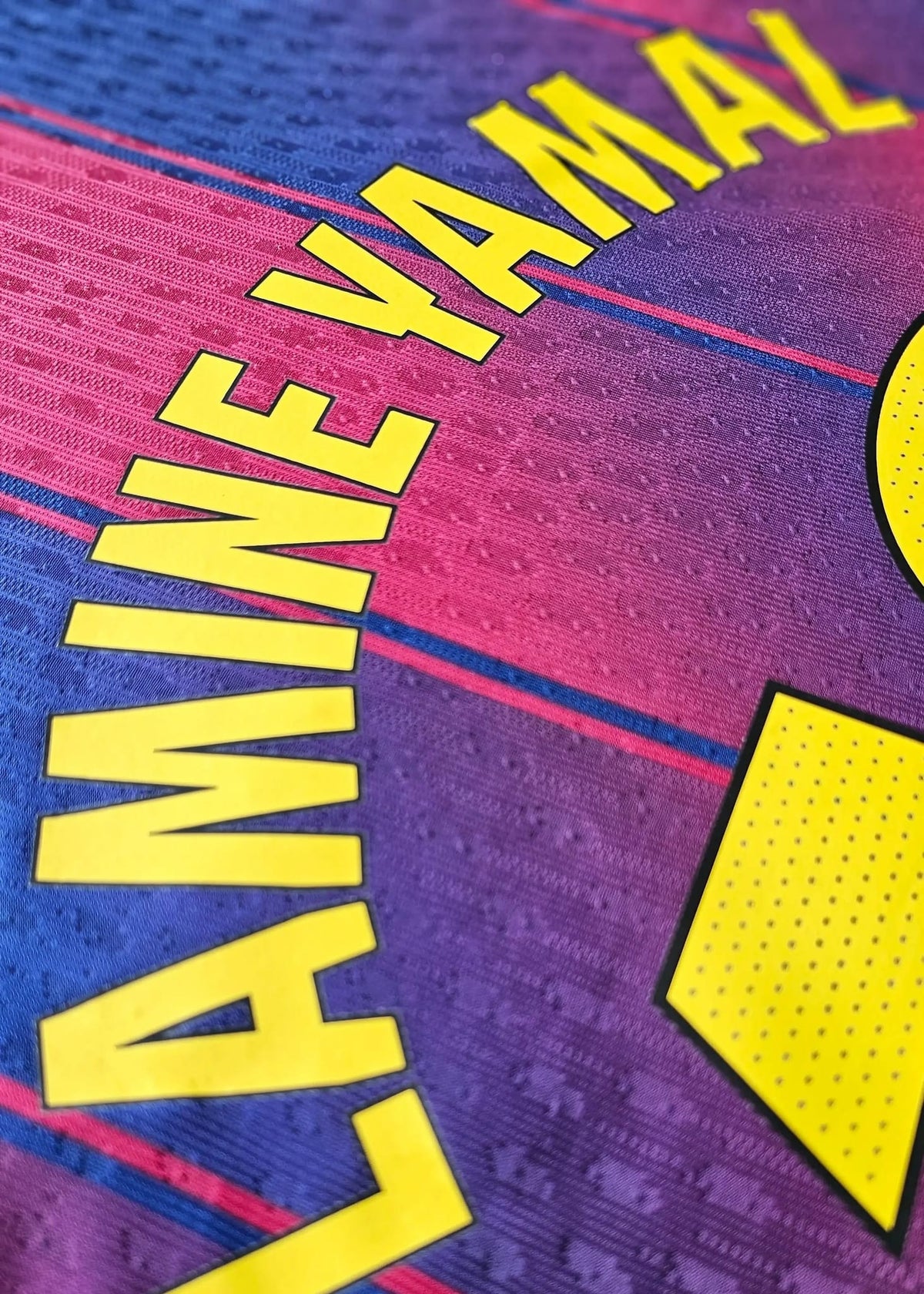 The partial yellow 'AMINE YAMAL' nameset and the edge of the number 10, printed on the blue and maroon striped FC Barcelona 2025-2026 shirt.