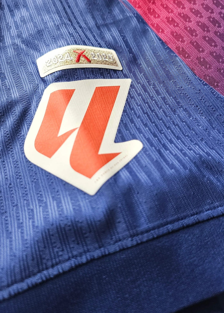 A gold '2024 X 2025' season tab above an orange-and-white angular badge patch, stitched onto the royal blue sleeve fabric of the FC Barcelona size-L shirt.