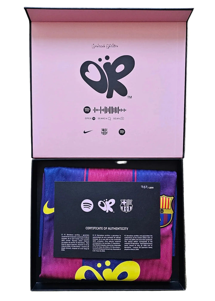 An open presentation box, containing a folded multicolor striped soccer jersey with yellow and blue accents, a black authenticity card, and branded packaging with a pink interior.