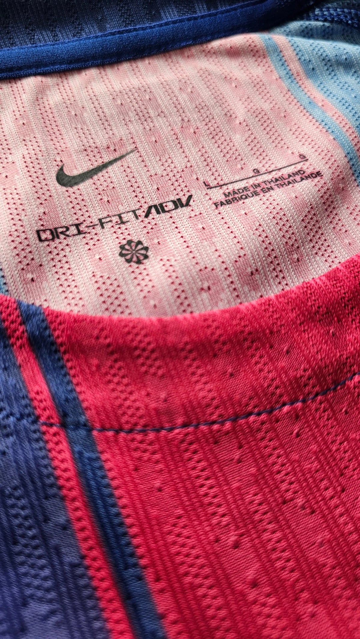 Close-up of a Nike athletic shirt showing the inner collar with a pink textured fabric, navy blue trim, and a red knit section. The inside label reads ORI-FIT/ADV and shows the Nike swoosh.