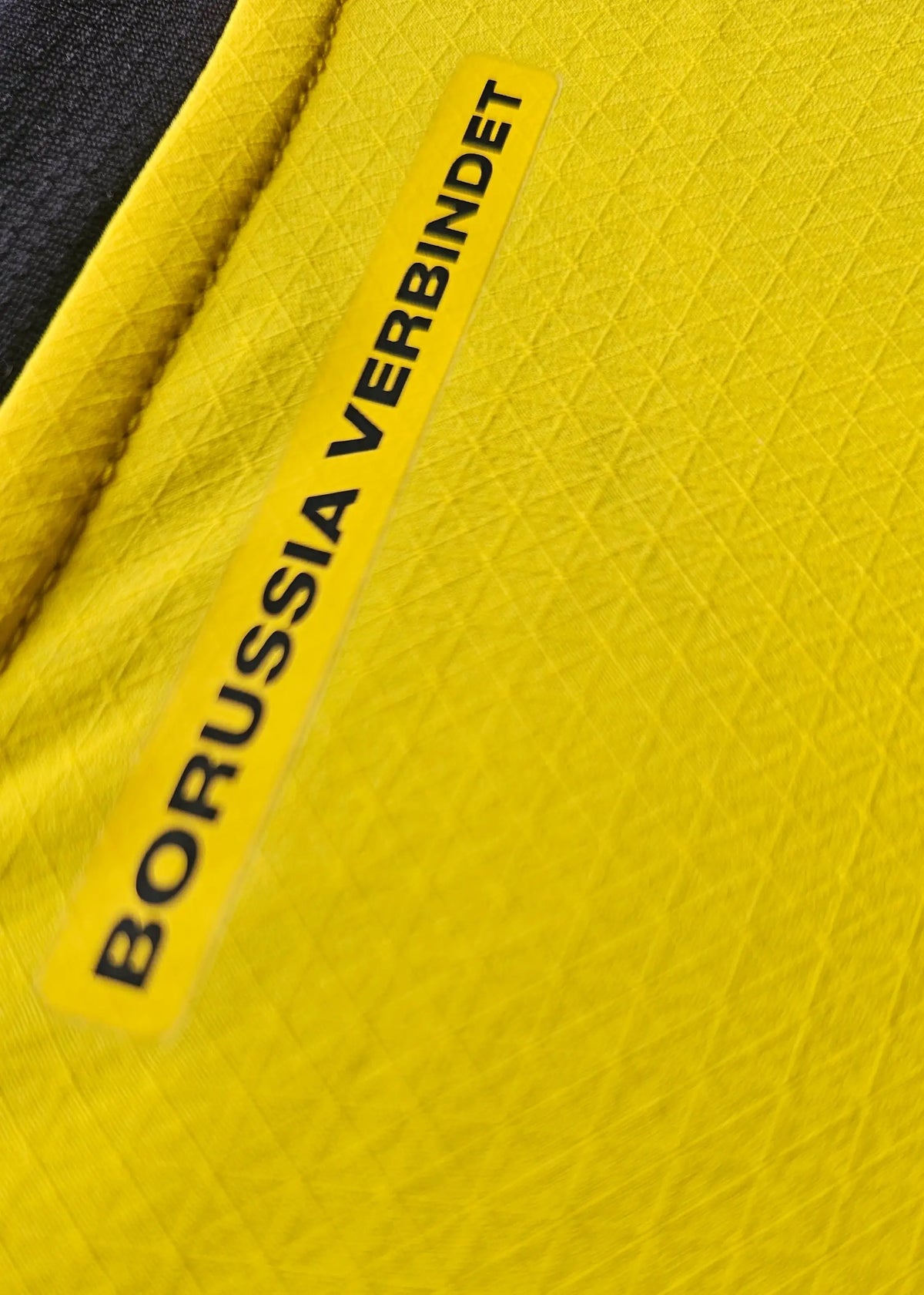A close-up highlights the 'Borussia verbindet' neck tag stitched into the yellow collar of this Mathis Albert Dortmund home shirt.