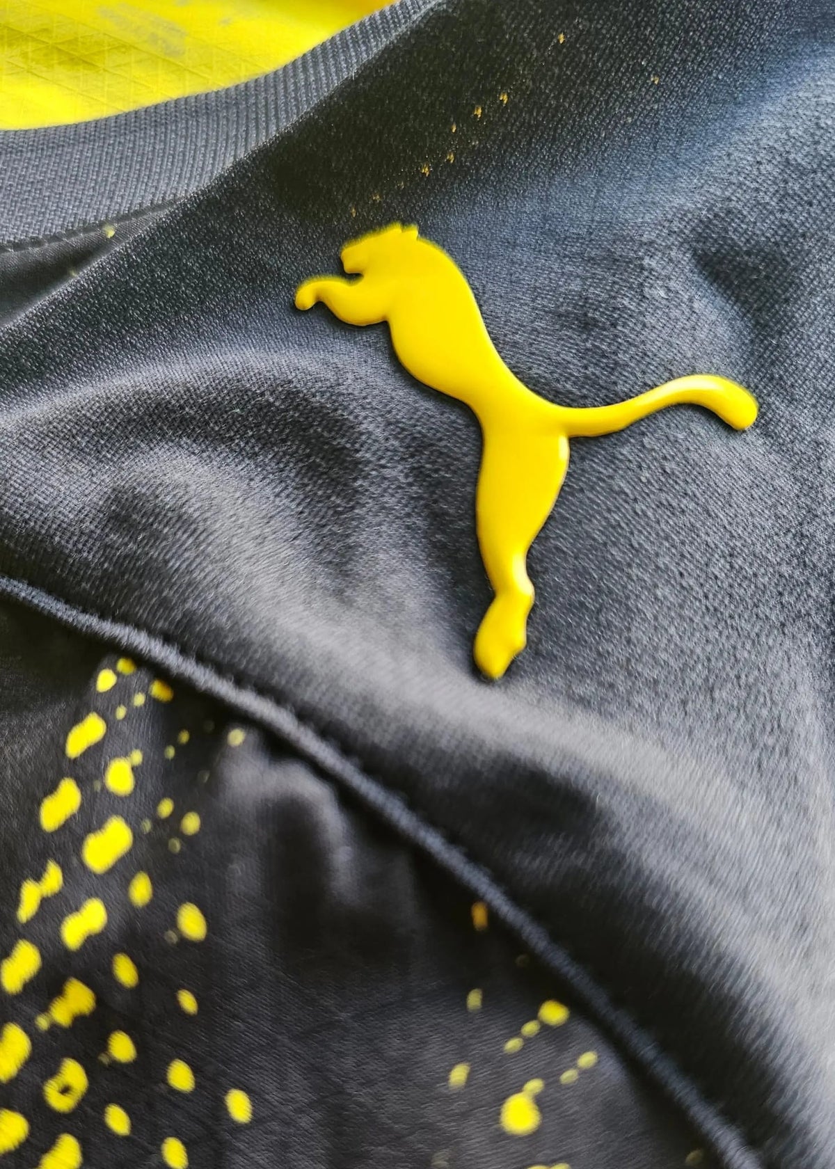 A yellow Puma cat logo is stitched onto the dark grey underside of the Borussia Dortmund shirt's collar.