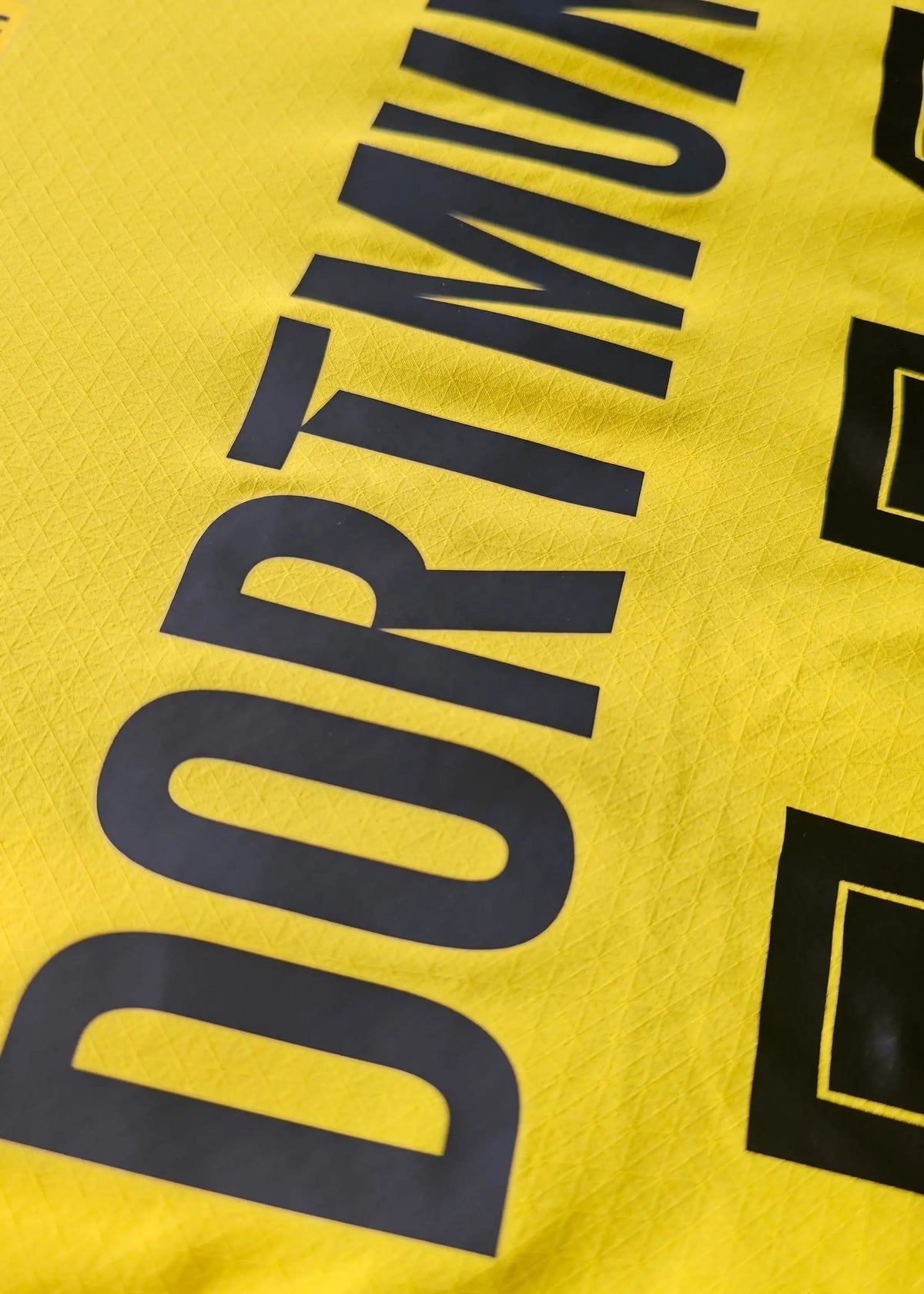 The DORTMUND wordmark is printed in black lettering across the yellow Borussia Dortmund home shirt fabric.