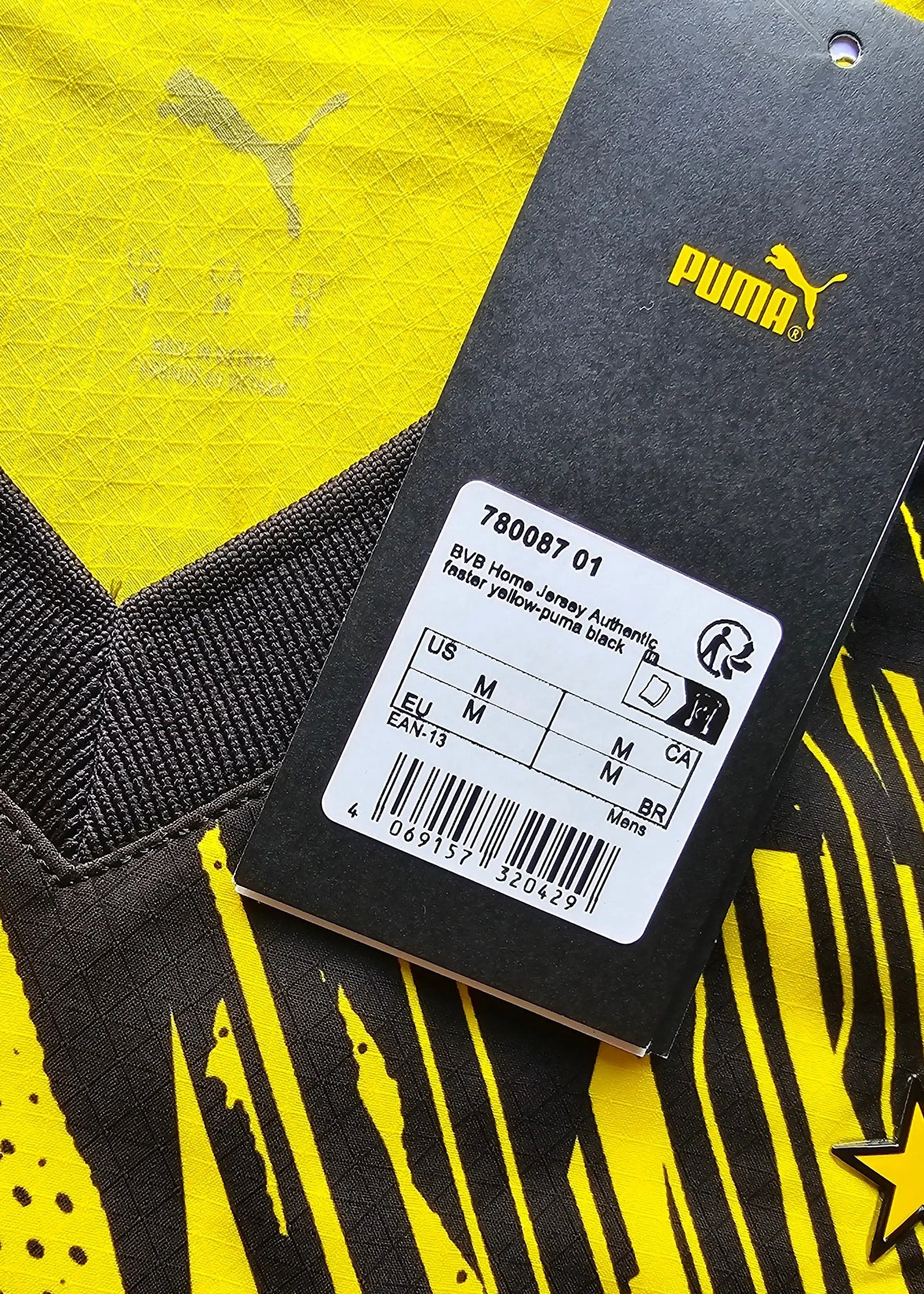 A Puma swing tag lists the BVB Home Jersey Authentic style, a size M and barcode, against the shirt's black sleeve.