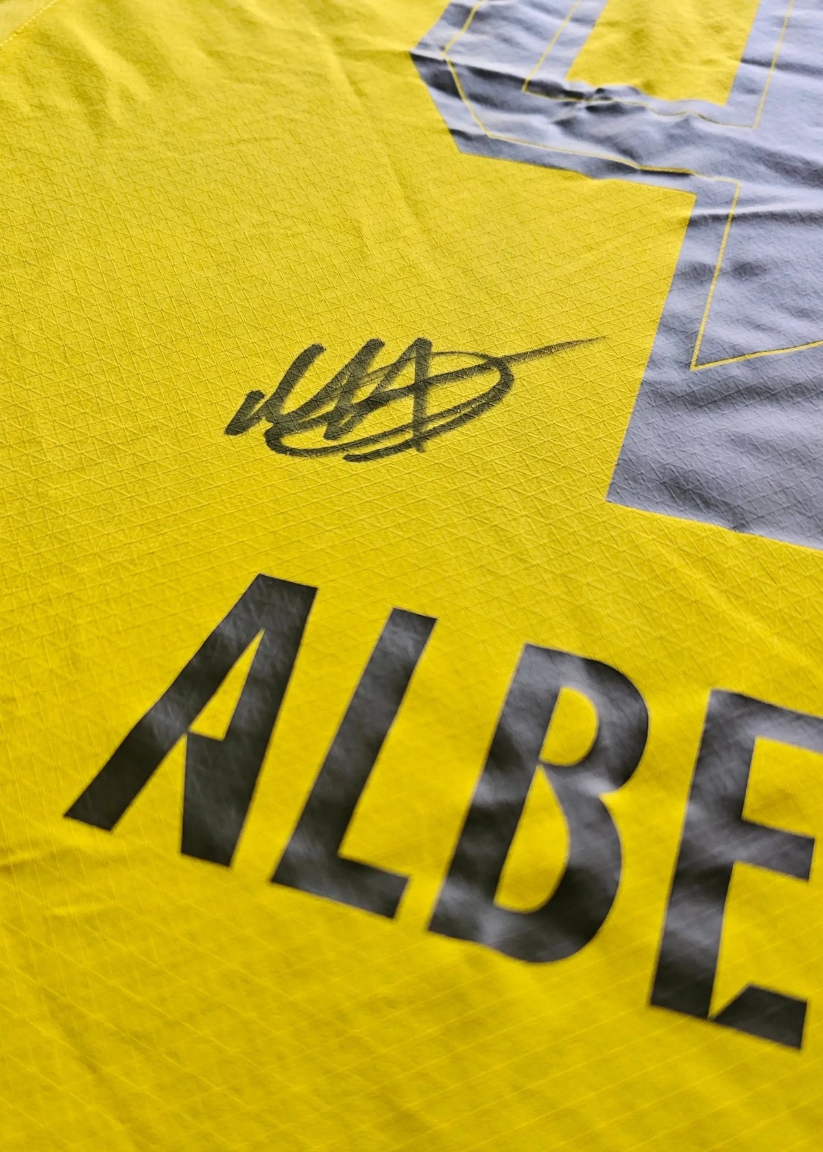 A close-up shows the black marker autograph on the yellow back panel of this Mathis Albert Dortmund 2025-26 home shirt.