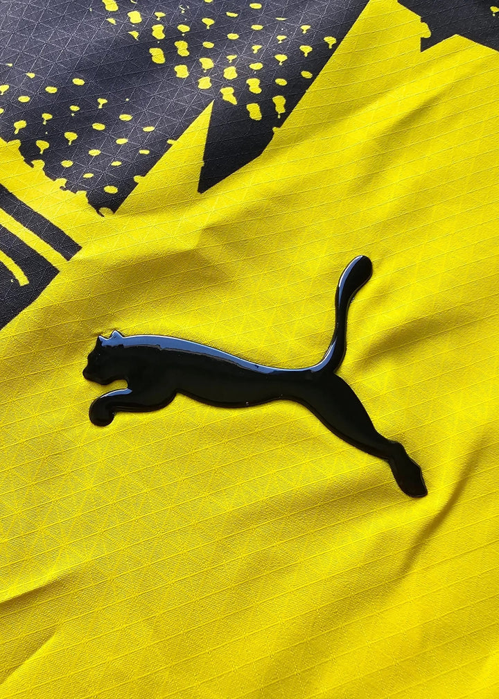 The black Puma cat logo contrasts with the yellow fabric and its jagged black star-burst graphic behind it.