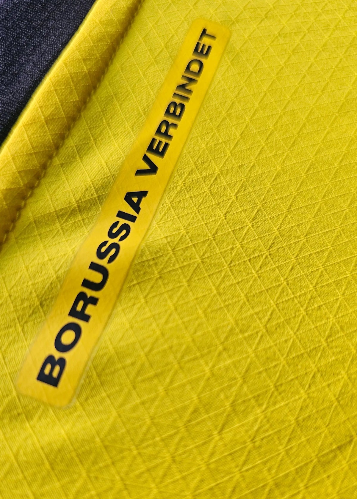 A vertical yellow tab reading Borussia Verbindet is stitched into the Borussia Dortmund shirt's side seam.