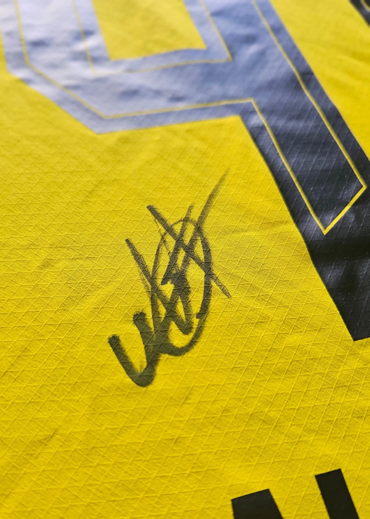 Close-up showing Mathis Albert's signature on a yellow football shirt with black detailing.