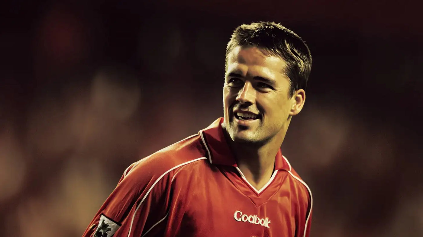 Michael Owen smiling match portrait in a classic red Liverpool shirt with a blurred stadium background
