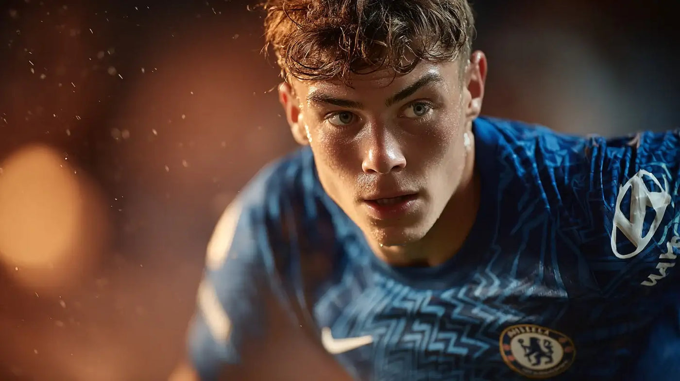 Ollie Harrison in Chelsea blue kit leaning forward in concentration under warm stadium lighting.