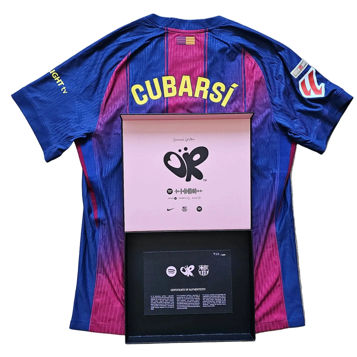 A blue and magenta striped FC Barcelona soccer jersey with 'CUBARSI' printed in yellow on the back, laid flat on a light wood floor with a framed award plaque placed in front of it.