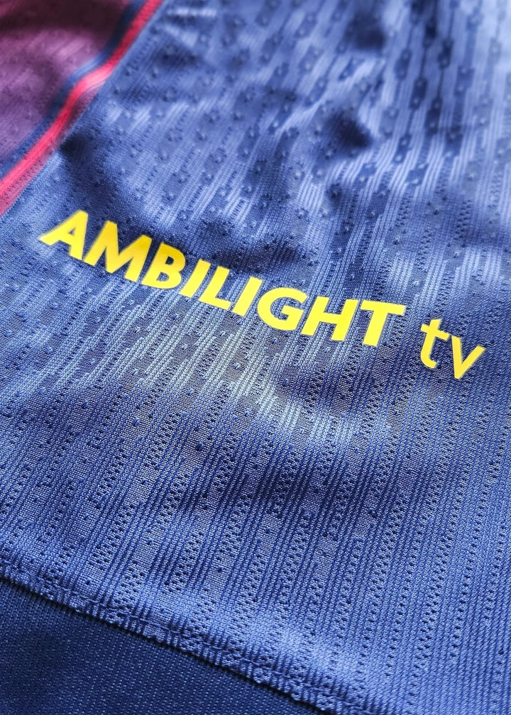 Yellow 'AMBILIGHT tv' sponsor wordmark printed on the blue fabric of Pau Cubarsí's FC Barcelona 2025-2026 shirt, No. 5.