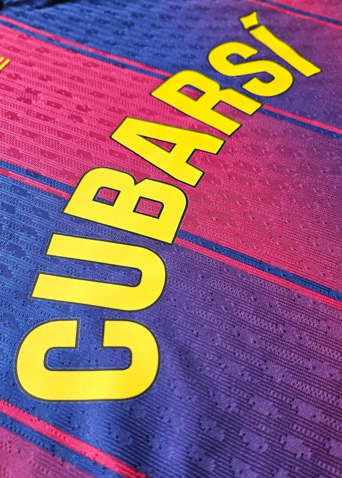 Yellow 'CUBARSI' nameset lettering printed on the blue and maroon striped fabric of the FC Barcelona 2025-2026 home shirt.