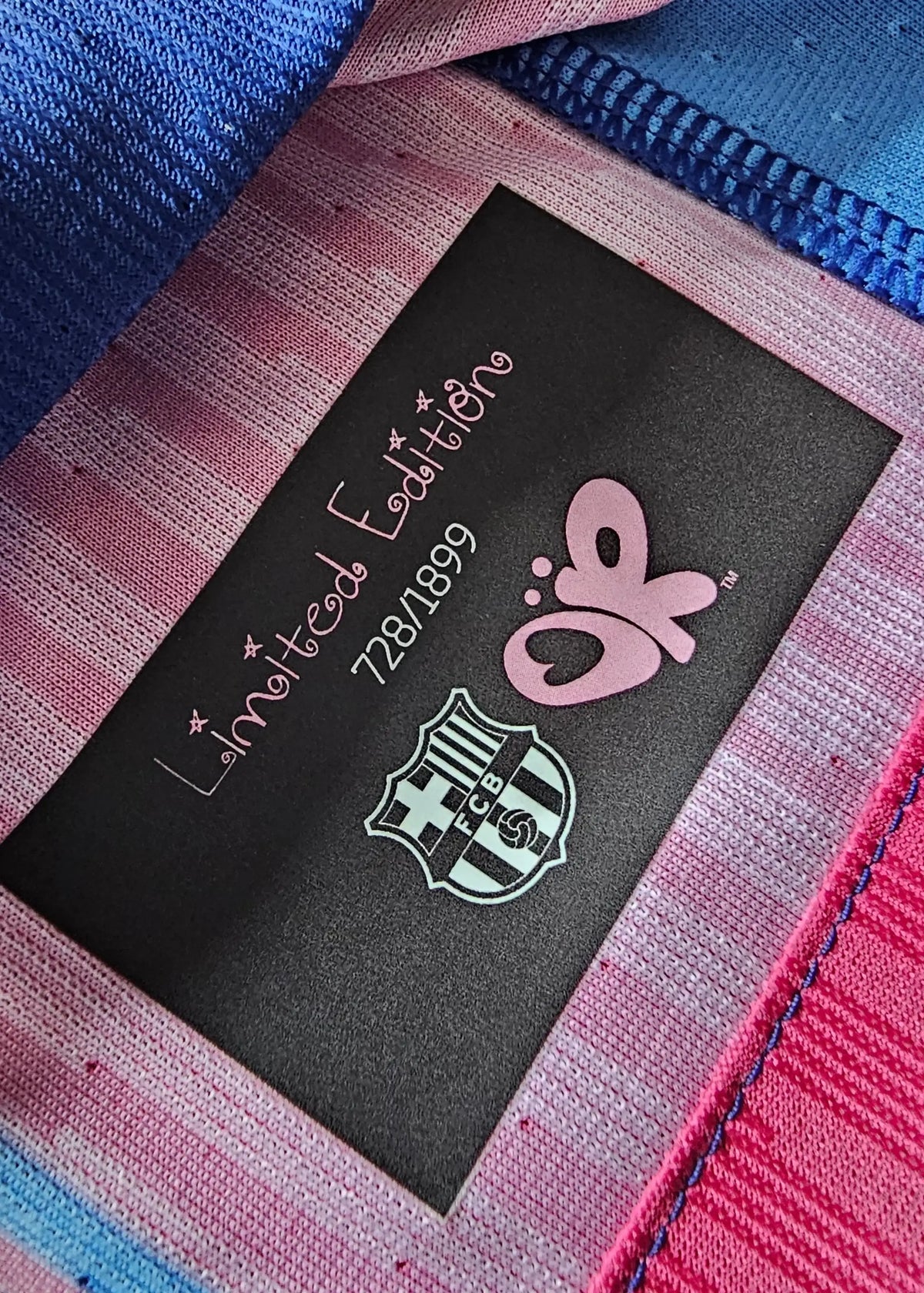 Black 'Limited Edition 728/1899' tag with the FC Barcelona crest and pink Olivia Rodrigo butterfly logo, sewn into Pau Cubarsí's shirt.