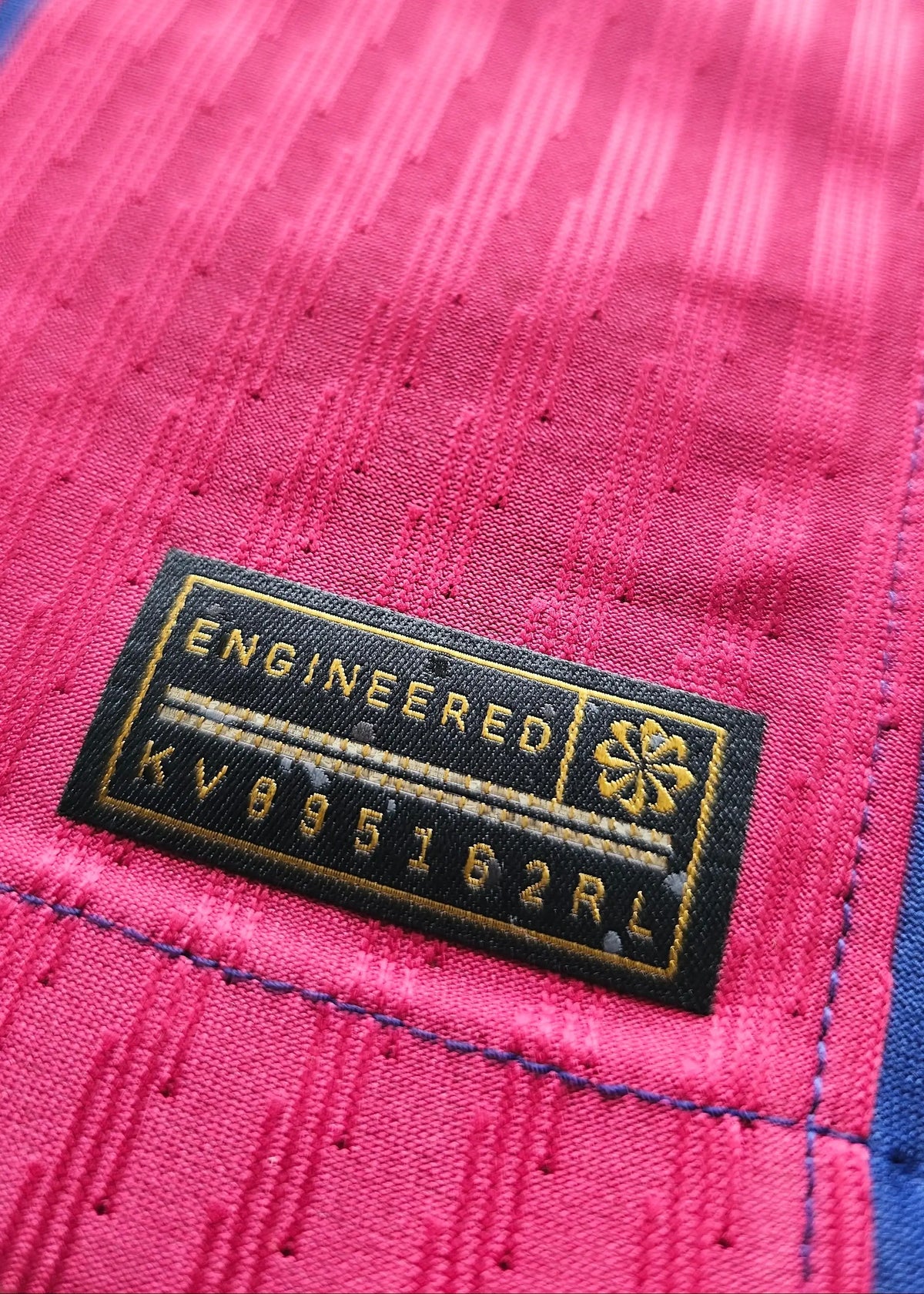 Black woven Nike 'Engineered' tag with a small gold emblem and style code KV095162RL, stitched onto the pink fabric of Pau Cubarsí's FC Barcelona shirt.