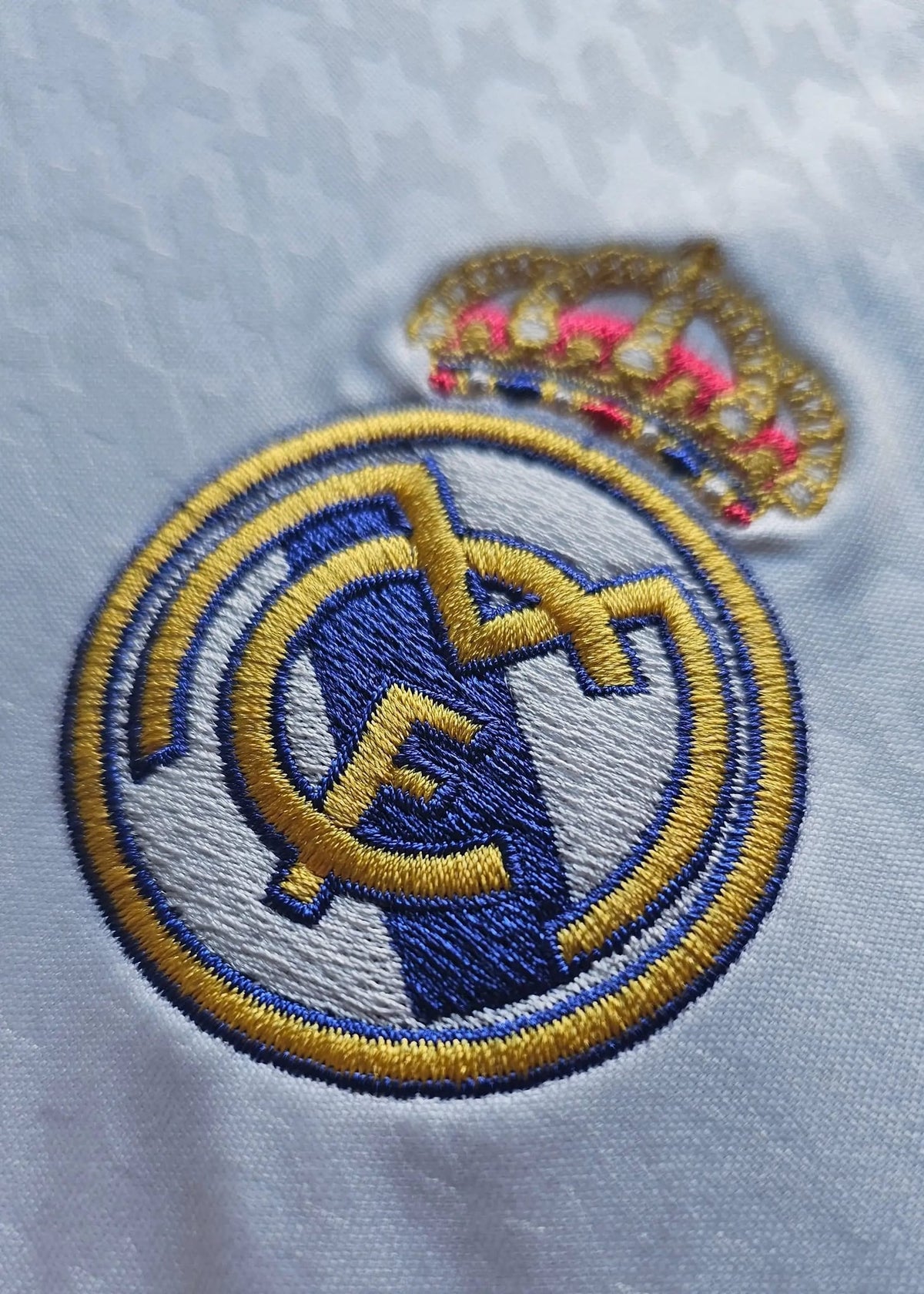 A close-up of the embroidered Real Madrid crest and crown on this Raul Asencio 2024-2025 home shirt, showing the fine gold and blue stitching.