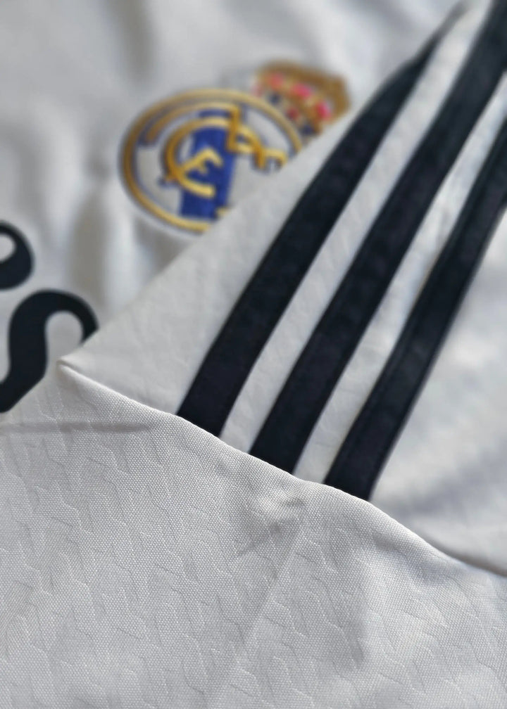 The Real Madrid crest and crown sit beside the adidas three stripes in this close-up of the Raul Asencio 2024-2025 home shirt.