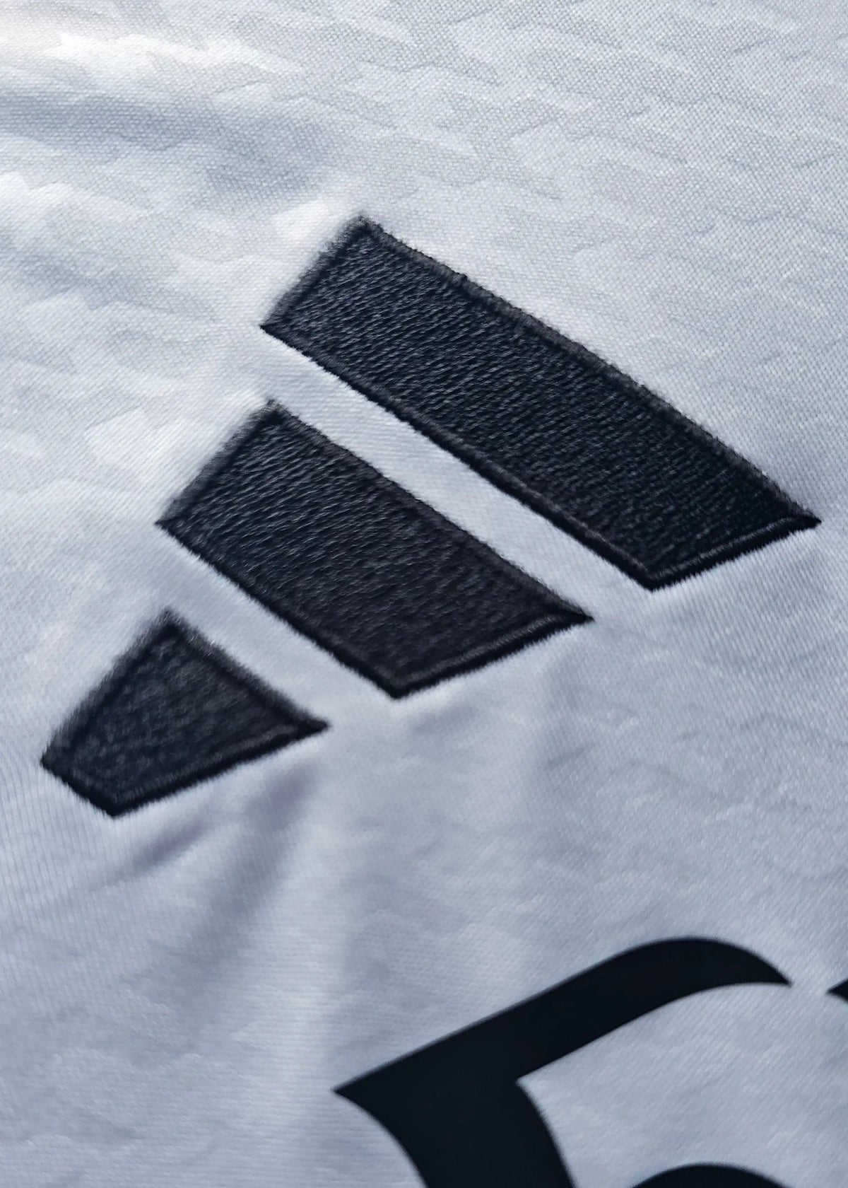 The adidas three-stripe logo on the shoulder seam of this Raul Asencio Real Madrid 2024-2025 No. 35 shirt, photographed in close-up.