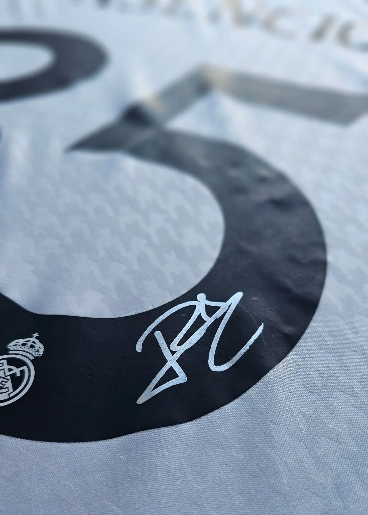 Detail showing No. 35 and Raúl Asencio's signature on a white football shirt with Real Madrid crest.