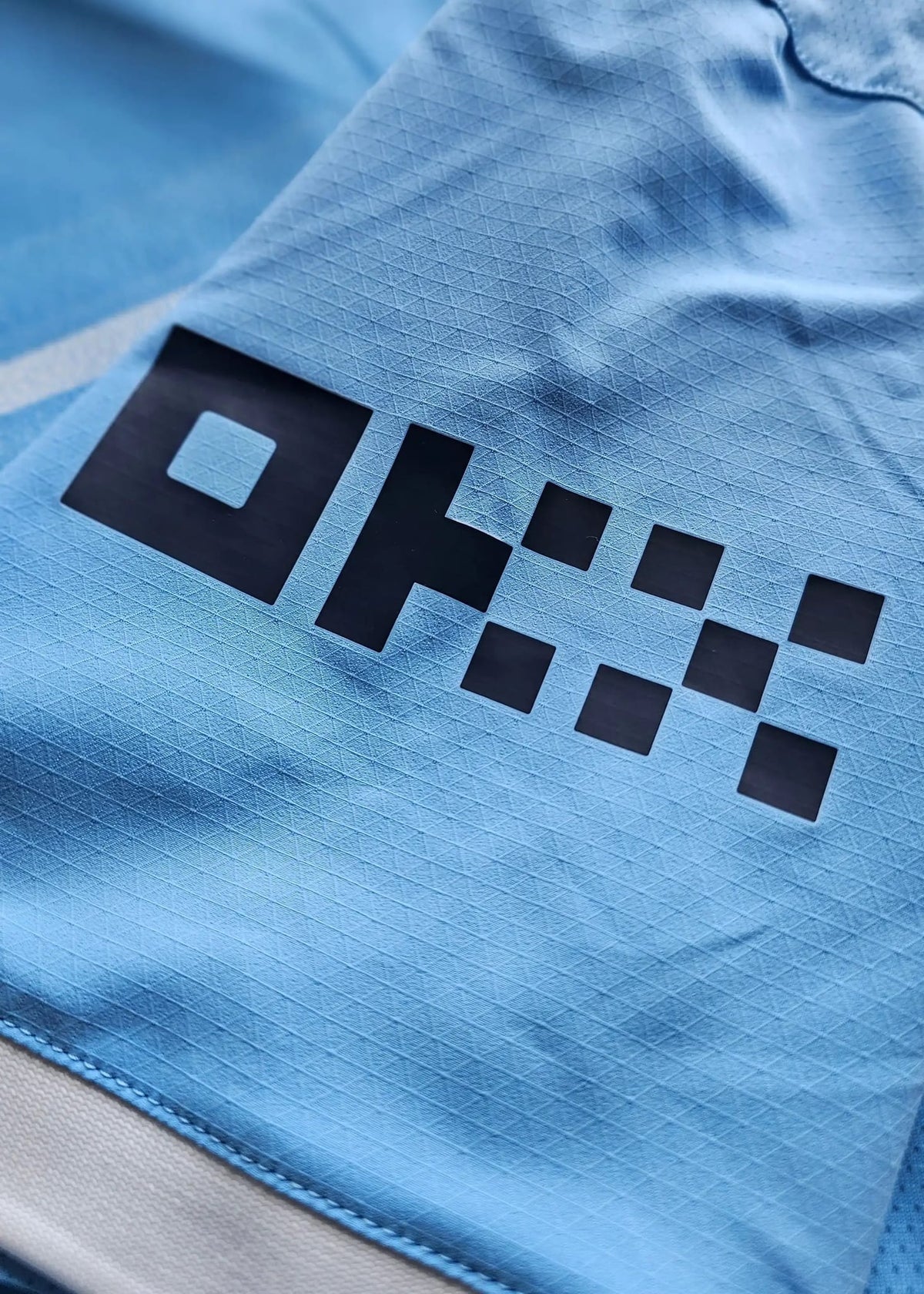 Close-up of a black checkerboard-diamond print on sky-blue fabric, from the signed Reigan Heskey Manchester City F.C. 2025-2026 shirt.