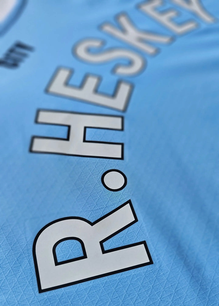 Close-up of the printed HESKEY lettering on sky-blue fabric, from the signed Reigan Heskey Manchester City F.C. 2025-2026 shirt.