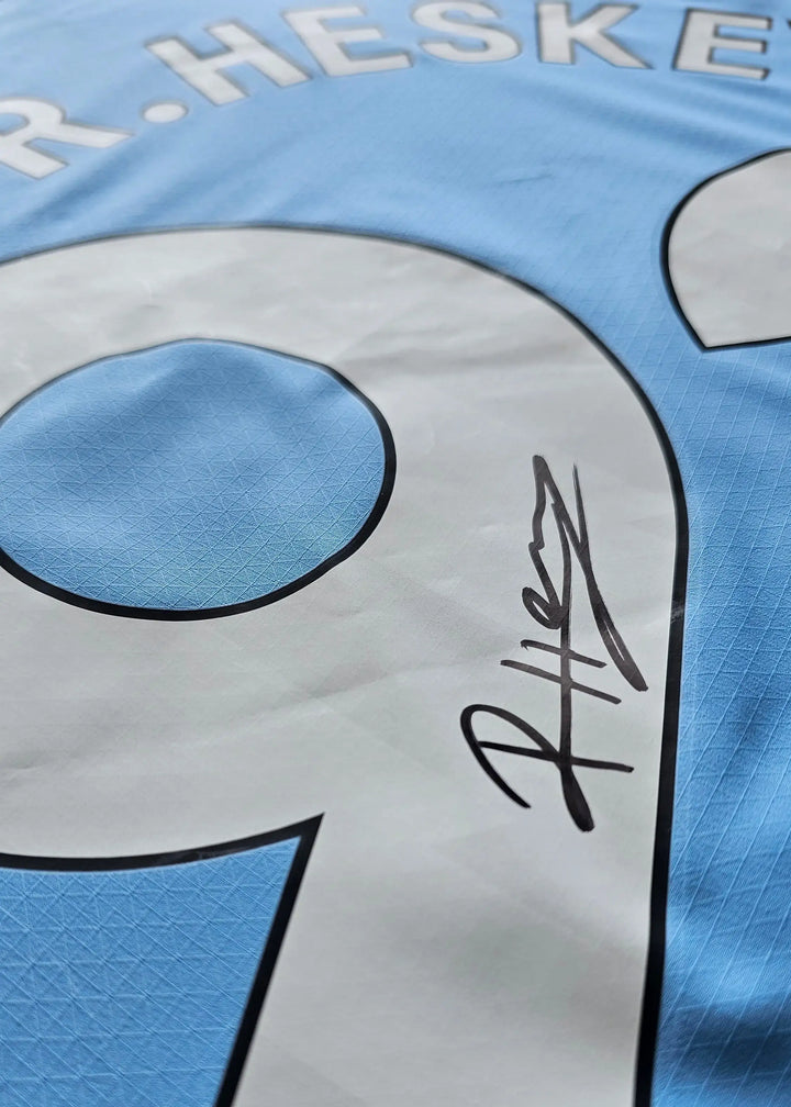 Close-up of a black signature beside the white No. 9 in HESKEY on a sky-blue Manchester City shirt, signed by Reigan Heskey.
