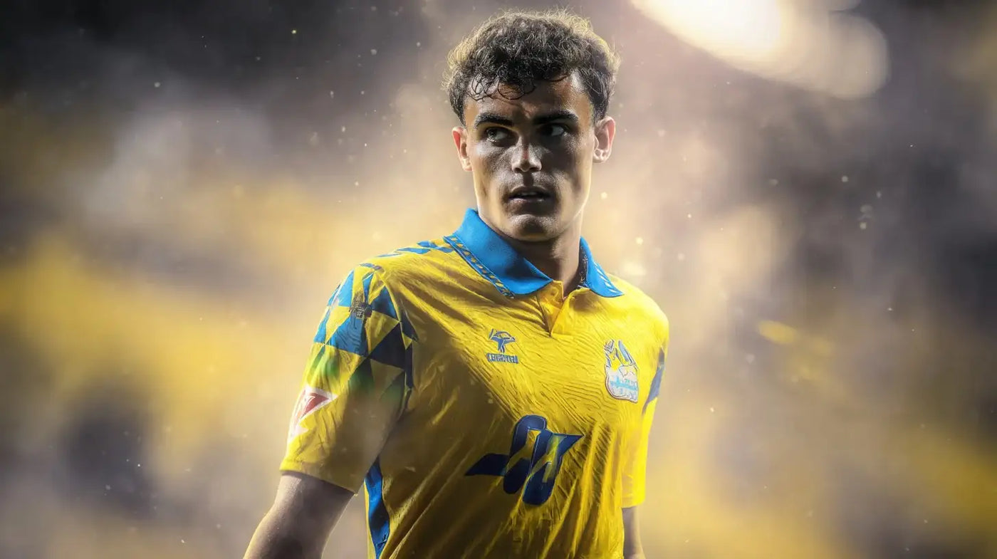 Stefan Bajcetic wearing a bright yellow Las Palmas football shirt with blue collar and geometric sleeve detail, looking to the side under glowing floodlights.
