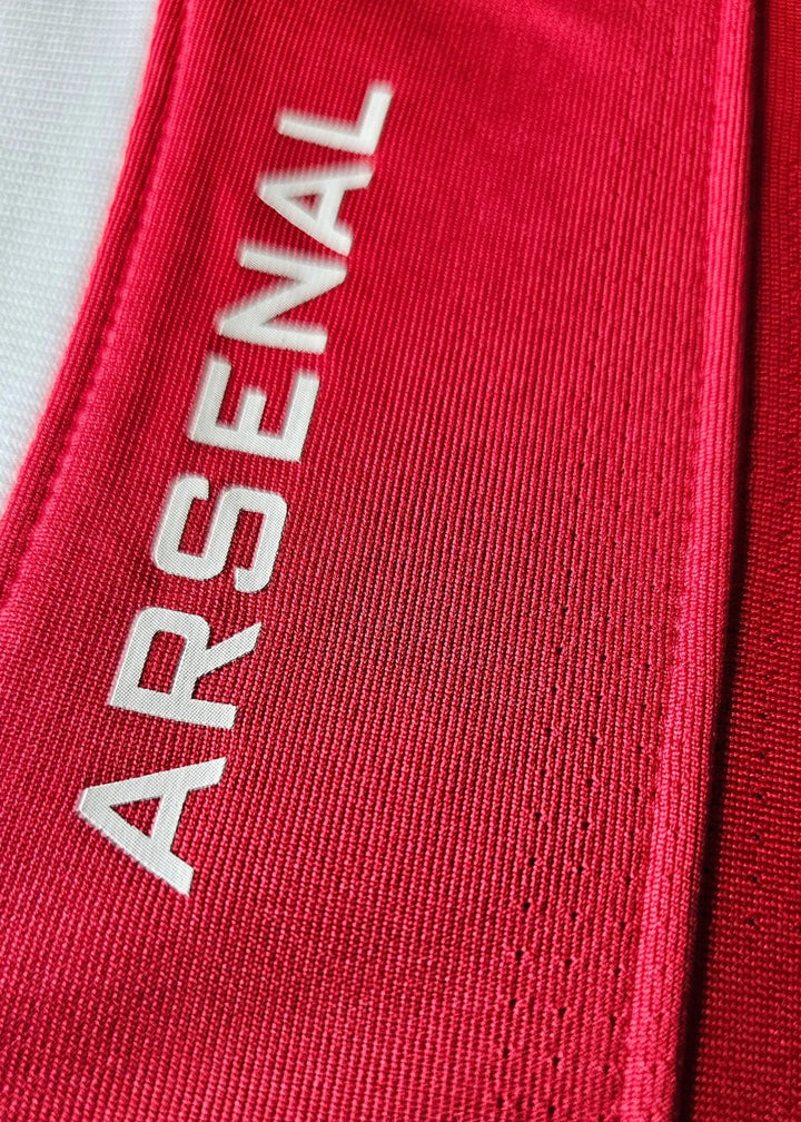 Close-up of a red textured fabric with the word ARSENAL printed vertically in white.