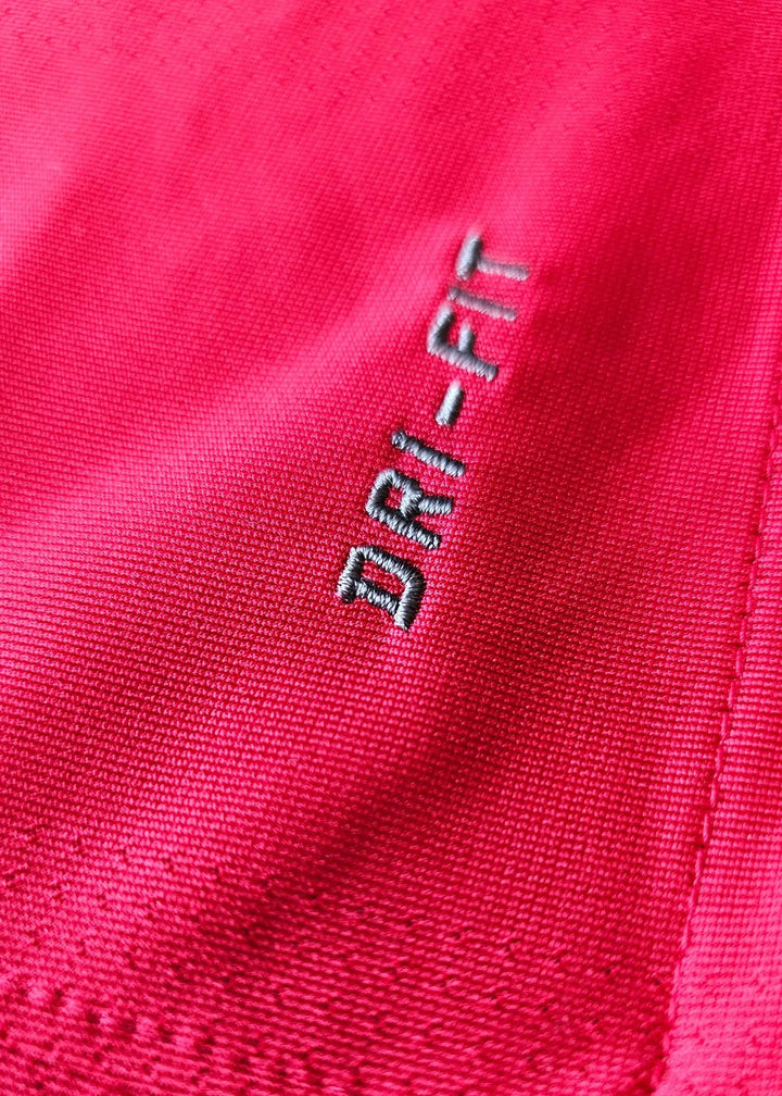 Close-up of the embroidered Nike DRI-FIT tag on red mesh fabric, from Robin van Persie's signed Arsenal 2010-11 No. 10 shirt.