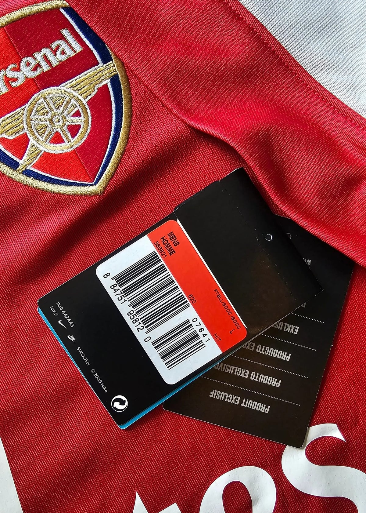 Arsenal crest beside a Nike swing tag with size and barcode details, resting on Robin van Persie's signed Arsenal 2010-11 No. 10 shirt.