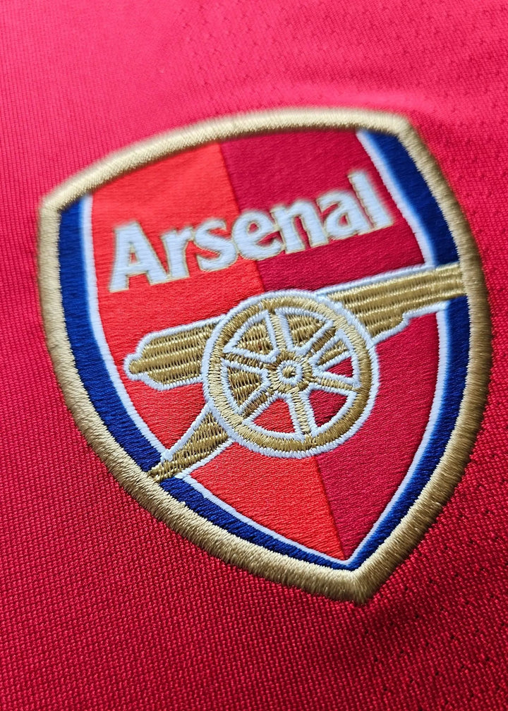 Arsenal crest with gold cannon and blue trim embroidered on the chest, from Robin van Persie's signed Arsenal 2010-11 No. 10 shirt.