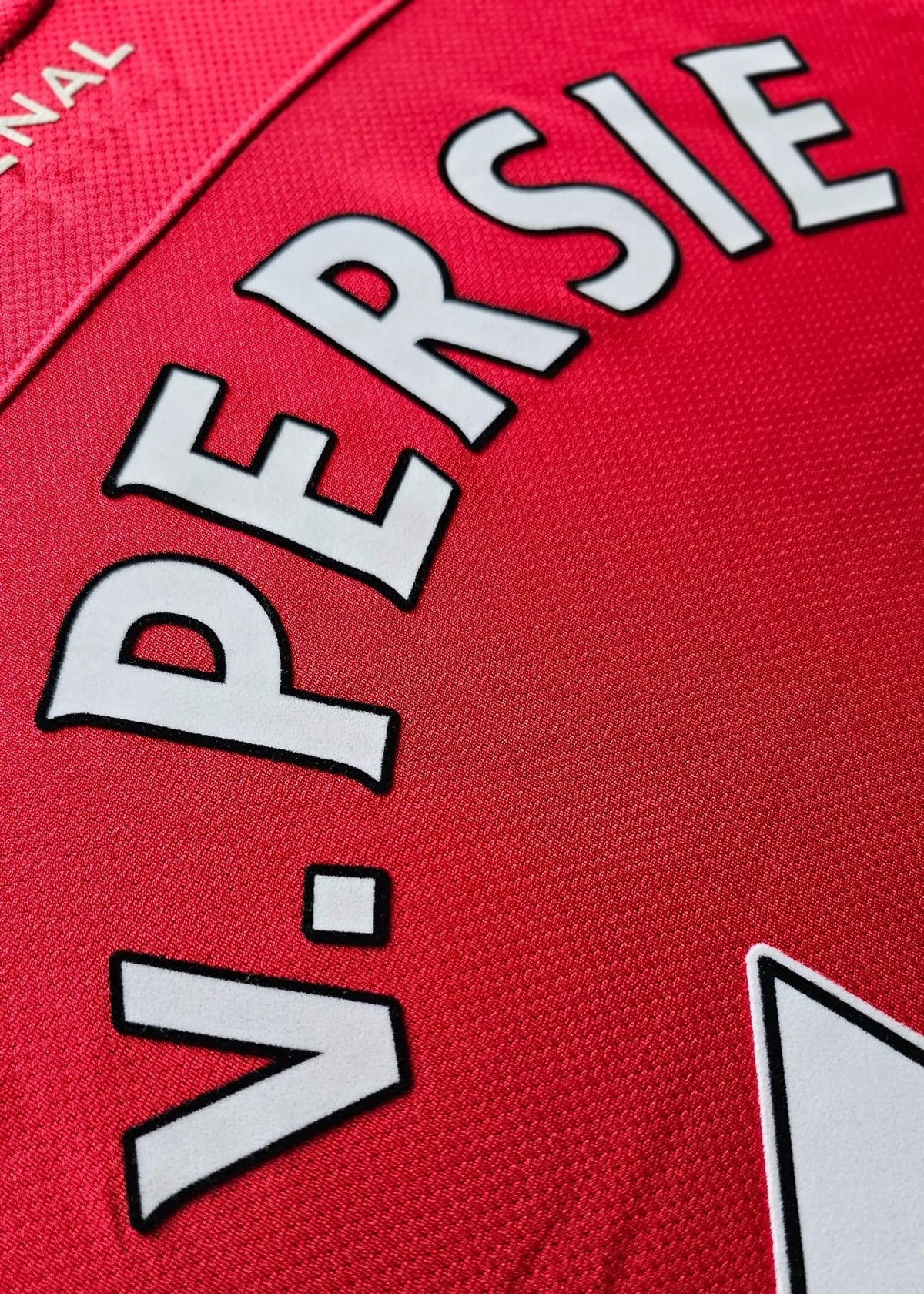 Close-up of a red sports jersey with large white lettering reading 'V. PERSIE' outlined in black, on a textured fabric background.