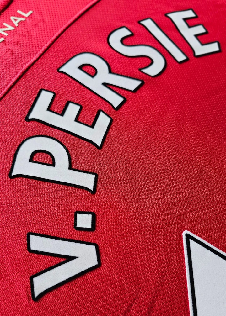 Close-up of a red sports jersey with large white lettering reading 'V. PERSIE' outlined in black, on a textured fabric background.