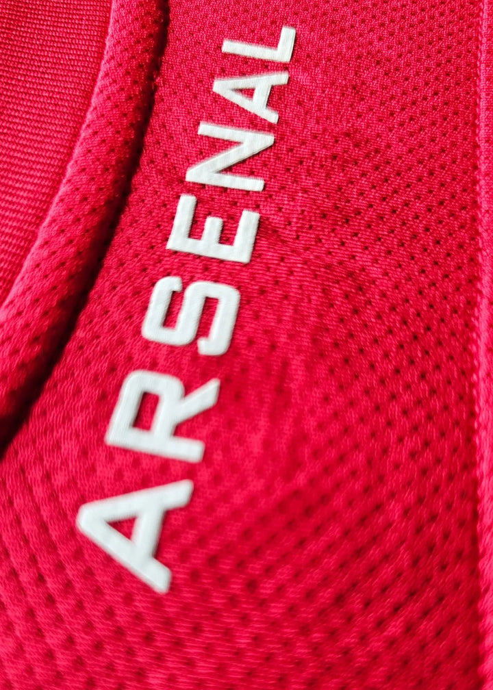 Close-up of the white ARSENAL wordmark running vertically on red shirt fabric near the collar, Robin van Persie's 2011-12 No. 10 shirt.