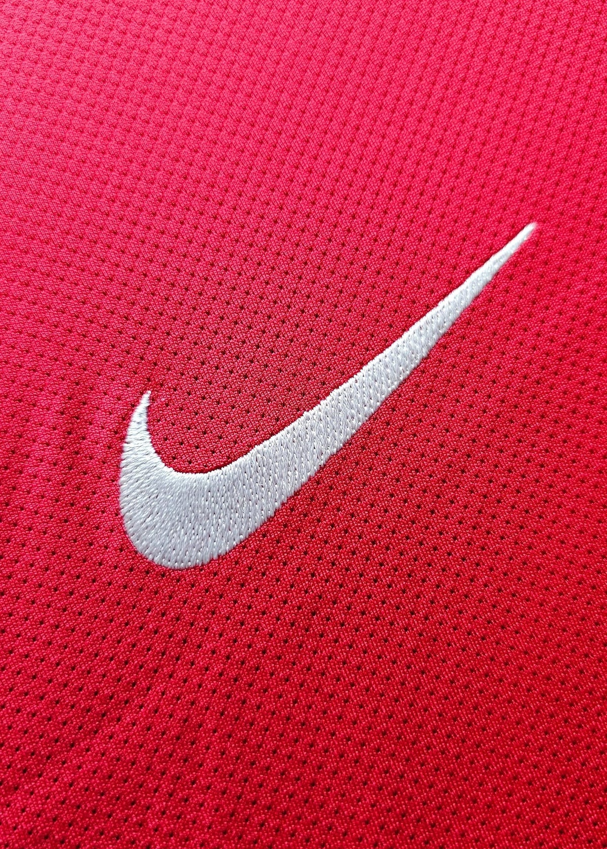 Close-up of the white Nike swoosh embroidered on red fabric, part of Robin van Persie's Arsenal 2011-12 No. 10 home shirt.