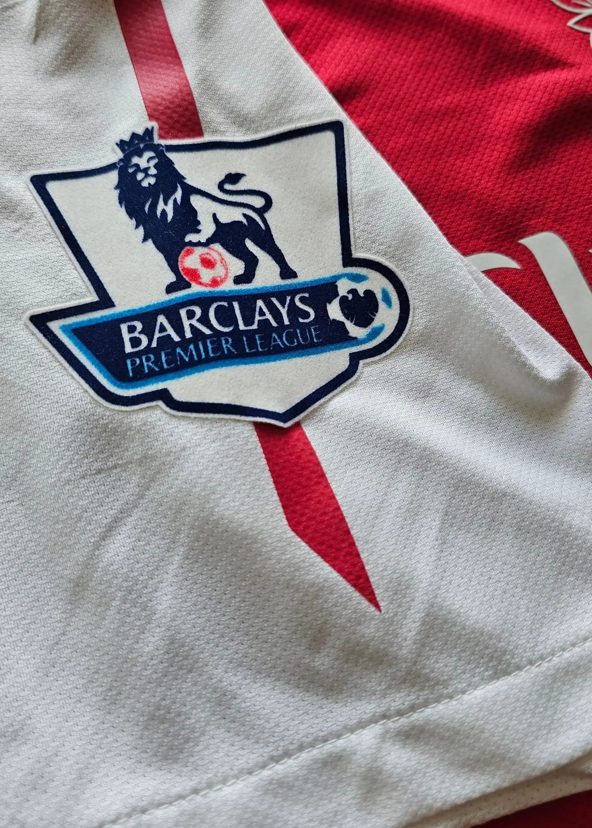 Close-up of the Barclays Premier League badge on white sleeve fabric with a red trim stripe, on Robin van Persie's 2011-12 Arsenal shirt.