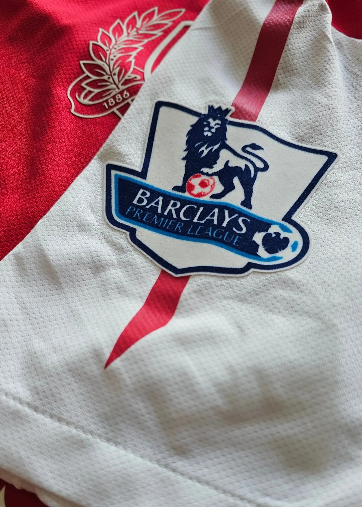 Close-up of the Barclays Premier League lion crest on the sleeve of a red and white Arsenal shirt, near the 1886 wreath emblem, No. 10.