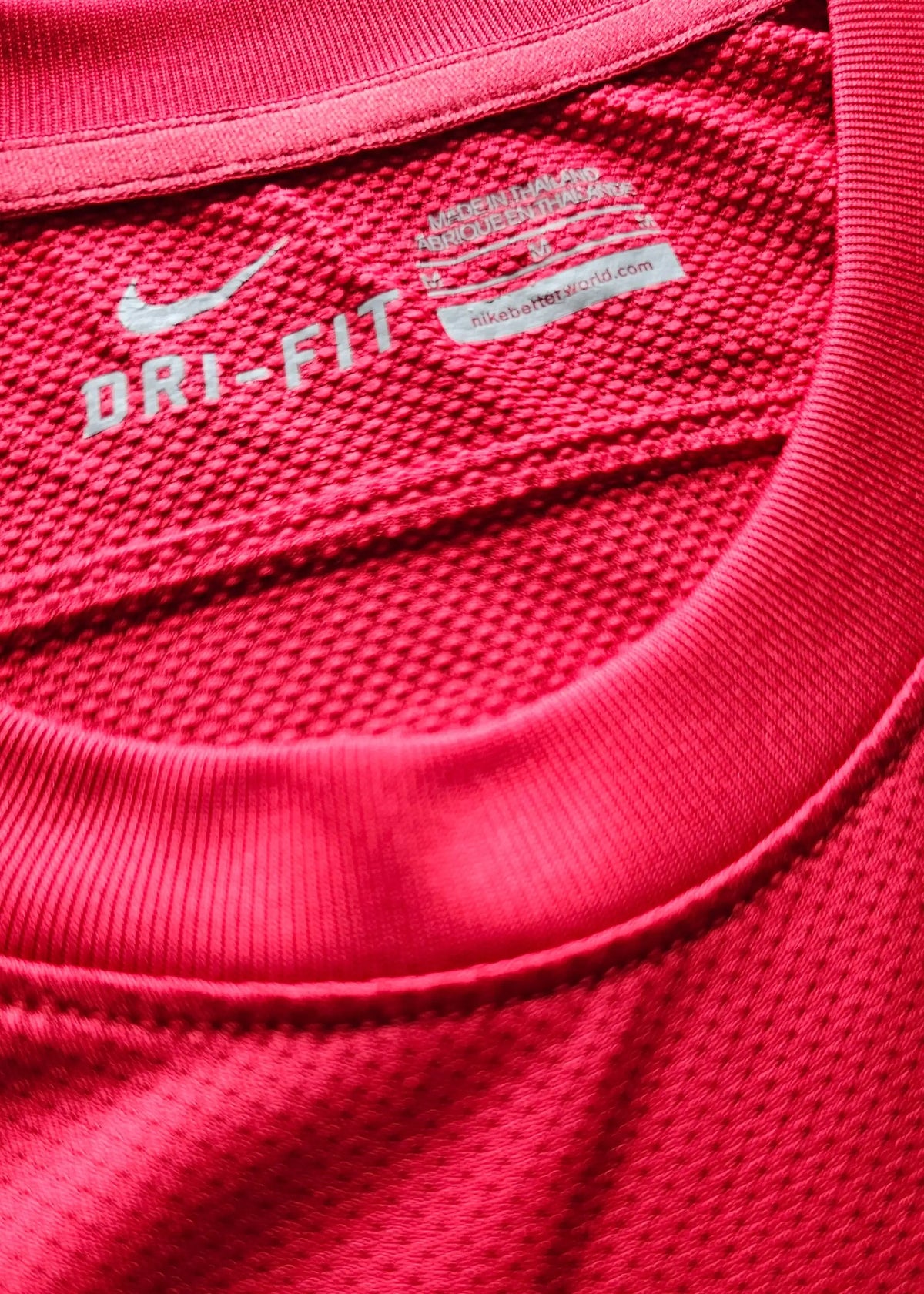 Close-up of the interior collar tag reading DRI-FIT with a Nike swoosh and made-in-Thailand text, inside Robin van Persie's red Arsenal shirt.