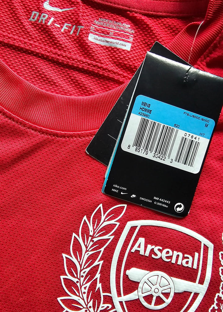 Interior collar tag reading DRI-FIT with the Nike swoosh, plus an attached retail swing tag with a barcode, Mens Homme M, beside the Arsenal crest.